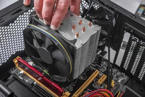 A technicians hand installs metal CPU cooler with a black fan onto a motherboard Stock Photos