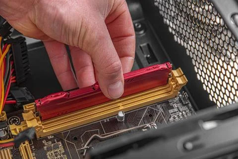 A technicians hand is shown installing a red RAM module into a motherboard slot Stock Photos