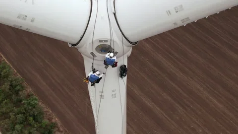 Technicians with harnesses go down wind turbine blade pylon Stock Footage 165202964