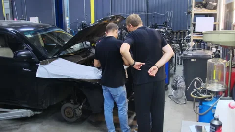 Technicians inspect engine compartment standing near hood of car Stock Footage 317632325