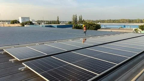 Technicians installing solar panel mounting rails on the metal roof of an ind Stock Photos