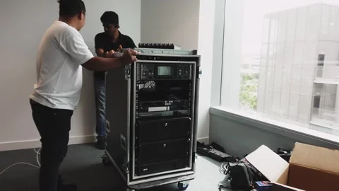 Technicians moving a portable server rack into position in an empty office Stock Footage 244787981