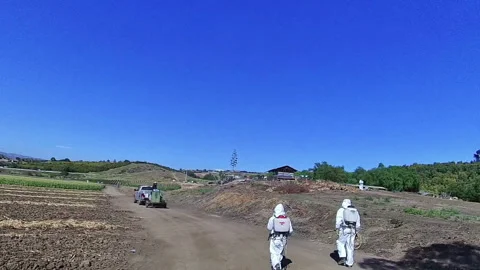 Technicians Walking Down Dirt Road wearing white chemical suits Stock Footage 277514412