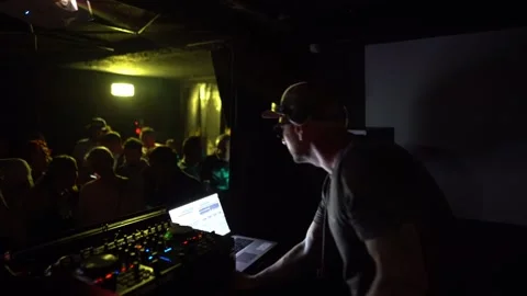 Techno DJ playing live set in underground nightclub with green stage lighting Stock Footage 331565915