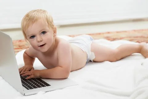 Technologically minded. Cute baby playing with a laptop while lying on the floor Stock Photos