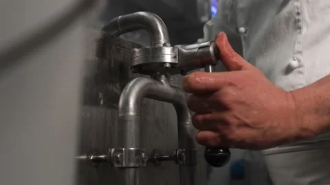 The technologist turns the handle of the milk supply valve on the metal cistern Stock Footage 145353235