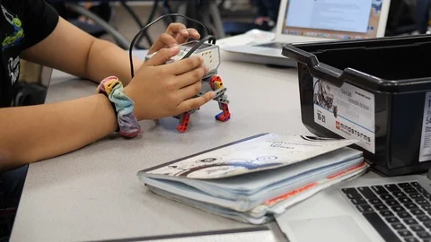 Technology Edu - Robot Walking Across Table Laptops Pan Right Stock Footage 126455696
