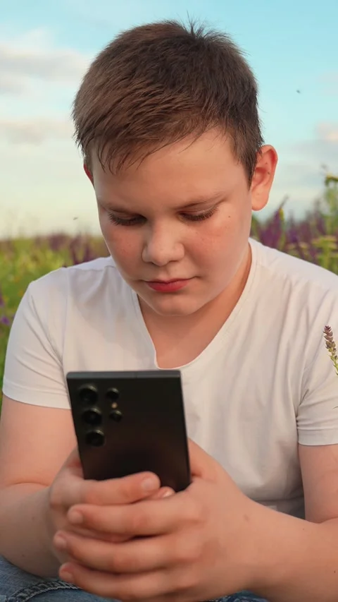 Technology in hands of boy, park lawn with flowers. Teenage boy plays on Stock-Footage 332249918