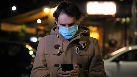 Technology, smartphone - man with mask types on his mobile in the city at night Stock-Footage 144756363