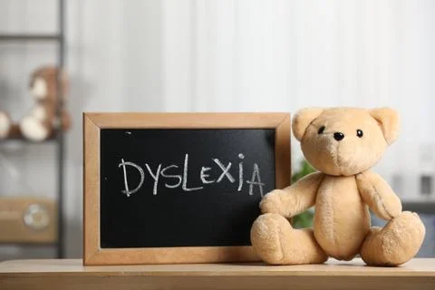 Teddy bear and small blackboard with word Dyslexia on wooden table in room Stock Photos