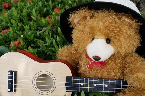 Teddy bear in a hat playing guitar in a flower garden background Foto stock