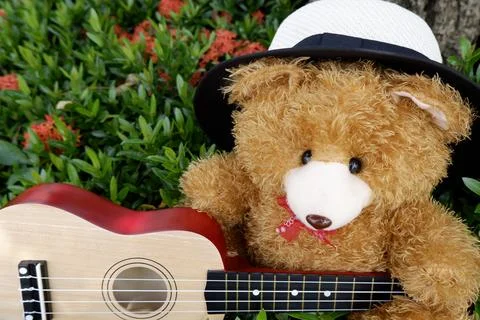 Teddy bear in a hat playing guitar in a flower garden background Stock Photos