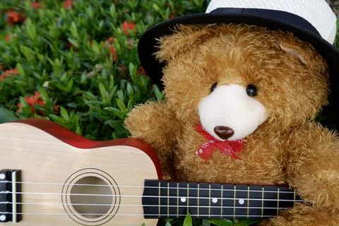 Teddy bear in a hat playing guitar in a flower garden background Foto stock