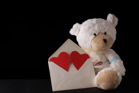 Teddy bear holding a big envelope with red hearts on black background Stock Photos