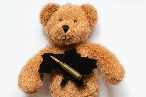 A teddy bear holding a black plastic 3D map of Ukraine and a bullet on a wh.. Stock Photos