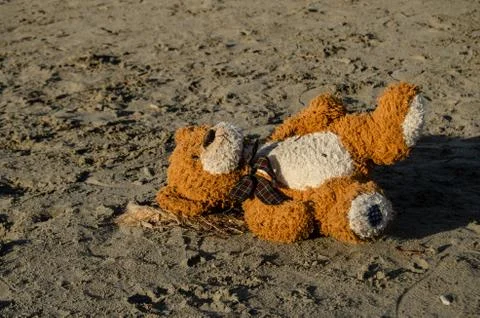 Teddy bear lying alone on the sand on the beach - abandoned, depresion, viole Stock Photos