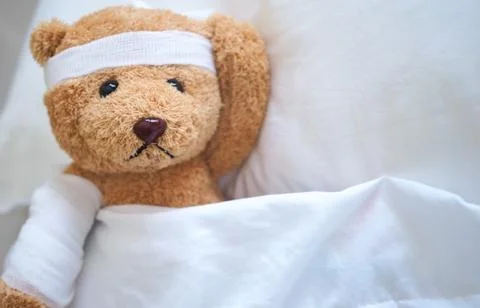 Teddy bear lying sick in bed With a headband and a cloth covered Foto stock