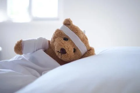 Teddy bear lying sick in bed With a headband and a cloth covered Stock Photos