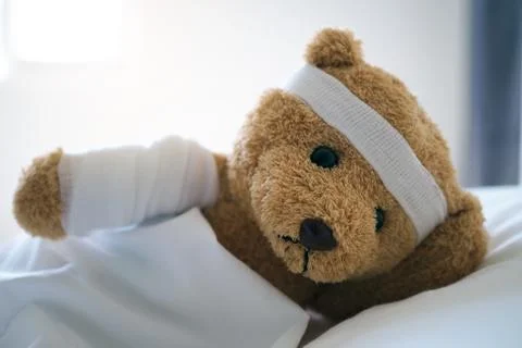 Teddy bear lying sick in bed With a headband and a cloth covered Foto stock
