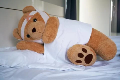 Teddy bear lying sick in bed With a headband and a cloth covered Foto stock