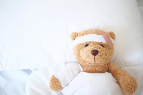 Teddy bear lying sick in bed With a headband and a cloth covered Foto stock