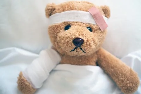 Teddy bear lying sick in bed With a headband and a cloth covered Foto stock