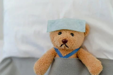 Teddy bear lying sick in bed. Teddy bear with antipyretic patch Foto stock