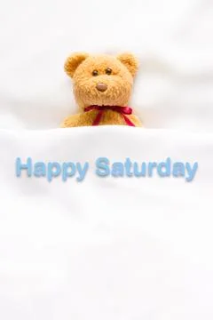 Teddy Bear lying in the white bed with message " Happy Saturday"  Stock Photos