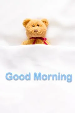 Teddy Bear lying in the white bed with message " Good morning " Stock Photos