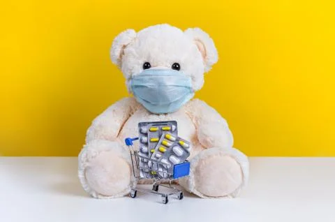 Teddy bear in medical mask and shopping cart with pills. Concept of illness,  Stock Photos