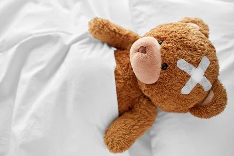 Teddy bear with medical patch on head lying in bed Foto stock