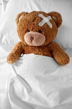 Teddy bear with medical patch on head lying in bed Foto stock