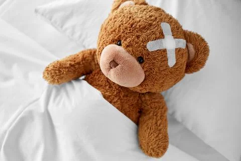Teddy bear with medical patch on head lying in bed Foto stock