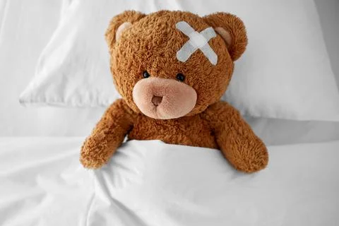 Teddy bear with medical patch on head lying in bed Foto stock