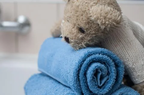 Teddy bear on rolled blue bath towels in bathroom Foto stock