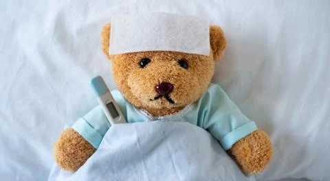 The teddy bear is sick on the bed with a high fever. There is a fever reducin Foto stock