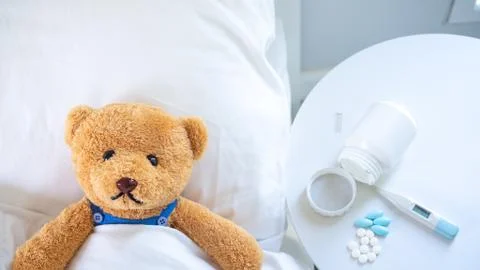 The teddy bear is sick in the bed next to him. There is medication, thermomet Stock Photos