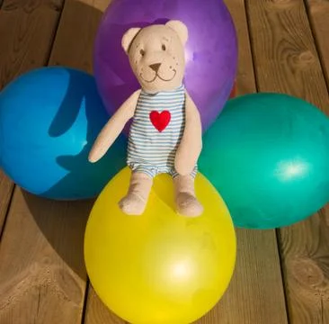Teddy bear sits on five balloons in different colors Stock Photos