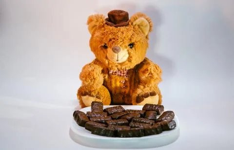 A teddy bear sits next to a plate of chocolad candy. Present Stock Photos