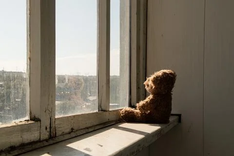 A teddy bear sits on the windowsill of an old apartment window, looking out,  Stock Photos