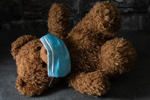 Teddy bear with surgical mask in dramatic light. Stock Photos