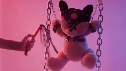 A Teddy bear suspended from chains in BDSM accessories is whipped on the body Video stock 138410960
