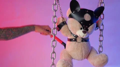 A Teddy bear suspended from chains in BDSM accessories is whipped on the body Stock Footage 138410972