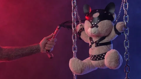 A Teddy bear suspended from chains in BDSM accessories is whipped on the body Video stock 138411004