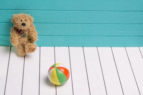 Teddy bear on a white wooden floor in blue-green background playing with ball Stock Photos