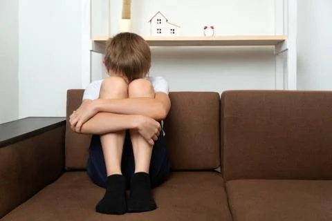 Teen boy sitting on couch with his arms around his knees. Domestic violence c Stock Photos