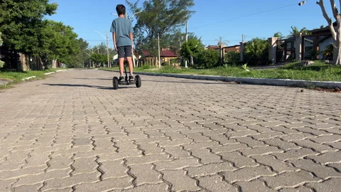 Teen boy steps onto hoverboard then rides away on residential street, 4K30 Video stock 331196053