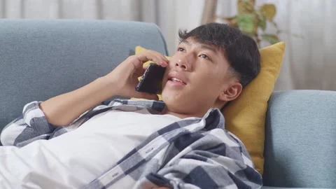 Teen Boy Talking On Smartphone While Lying On Sofa In The Living Room At Home Stock Footage 247982535