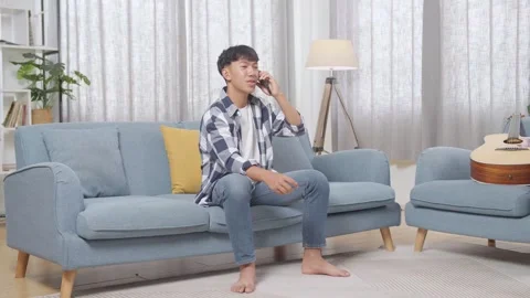 Teen Boy Talking On Smartphone While Sitting On Sofa In The Living Room At Home Stock Footage 247983647