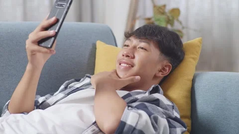 Teen Boy Using Smartphone Taking Selfie While Lying On Sofa In The Living Room Stock Footage 247982485